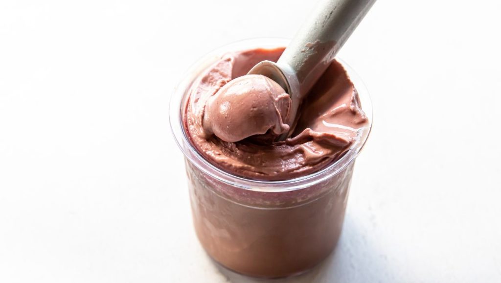 chocolate cherry ice cream in a clear pint with an ice cream scoop.