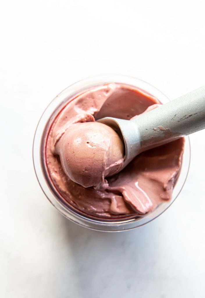 chocolate cherry ice cream in a clear pint with an ice cream scoop.