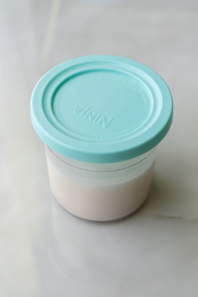 coconut ice cream in a ninja creami pint with a blue lid.