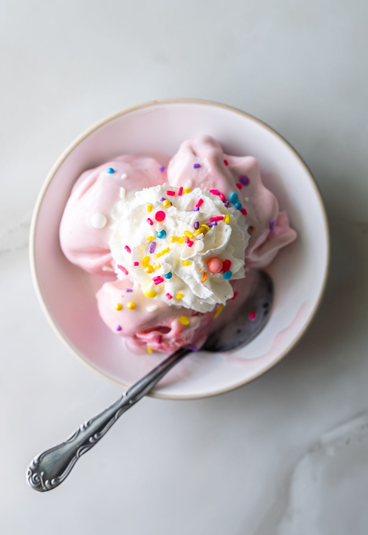 Ninja Creami strawberry ice cream in a bowl with whipped cream and sprinkles.