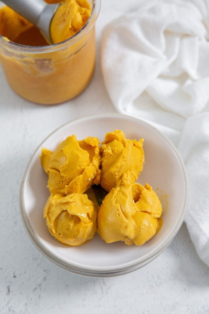 A bowl of creamy pumpkin ice cream sits invitingly with a spoon resting beside it, ready to be enjoyed.