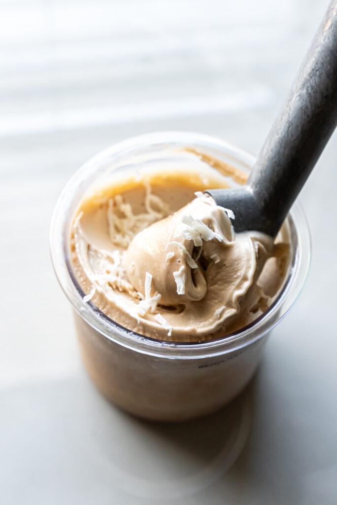 A spoon is scooping a rich scoop of Ninja Creami Pina Colada Protein Ice Cream, inviting a refreshing dessert moment.