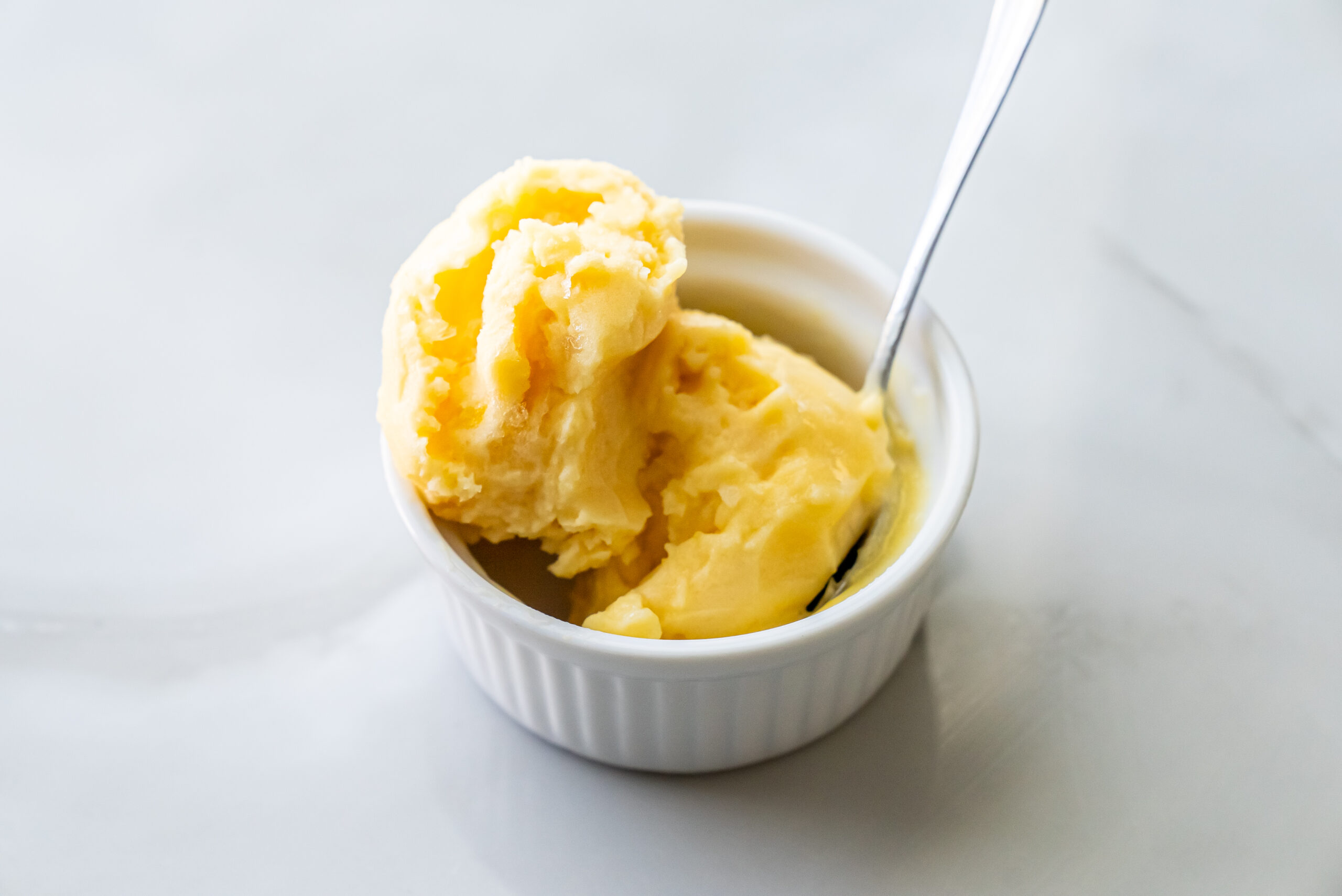 peach sorbet in a white bowl with a spoon.