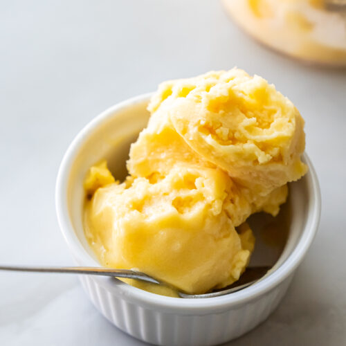 Ninja Creami peach sorbet in a white bowl with a spoon.