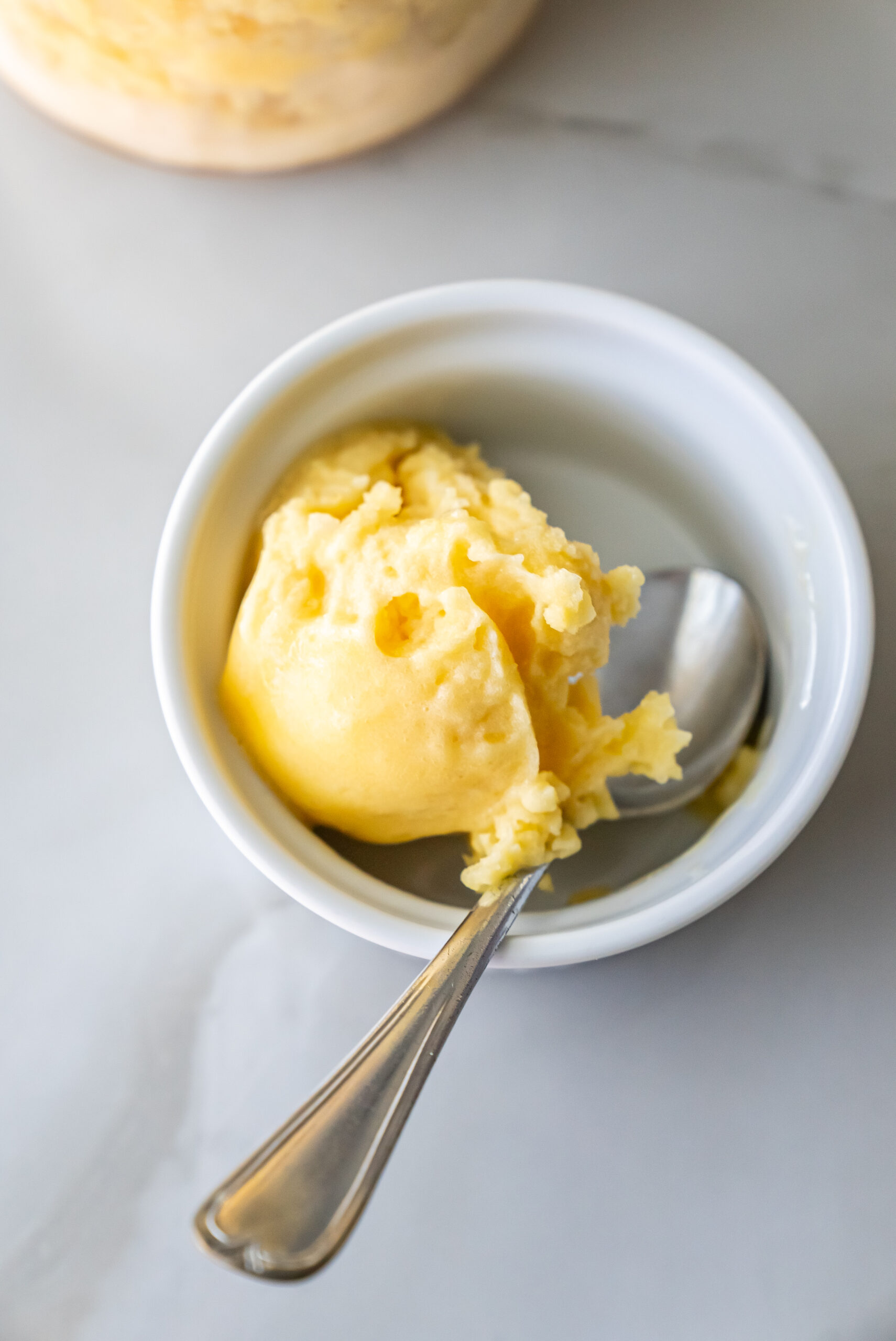 peach sorbet in a white bowl with a spoon.